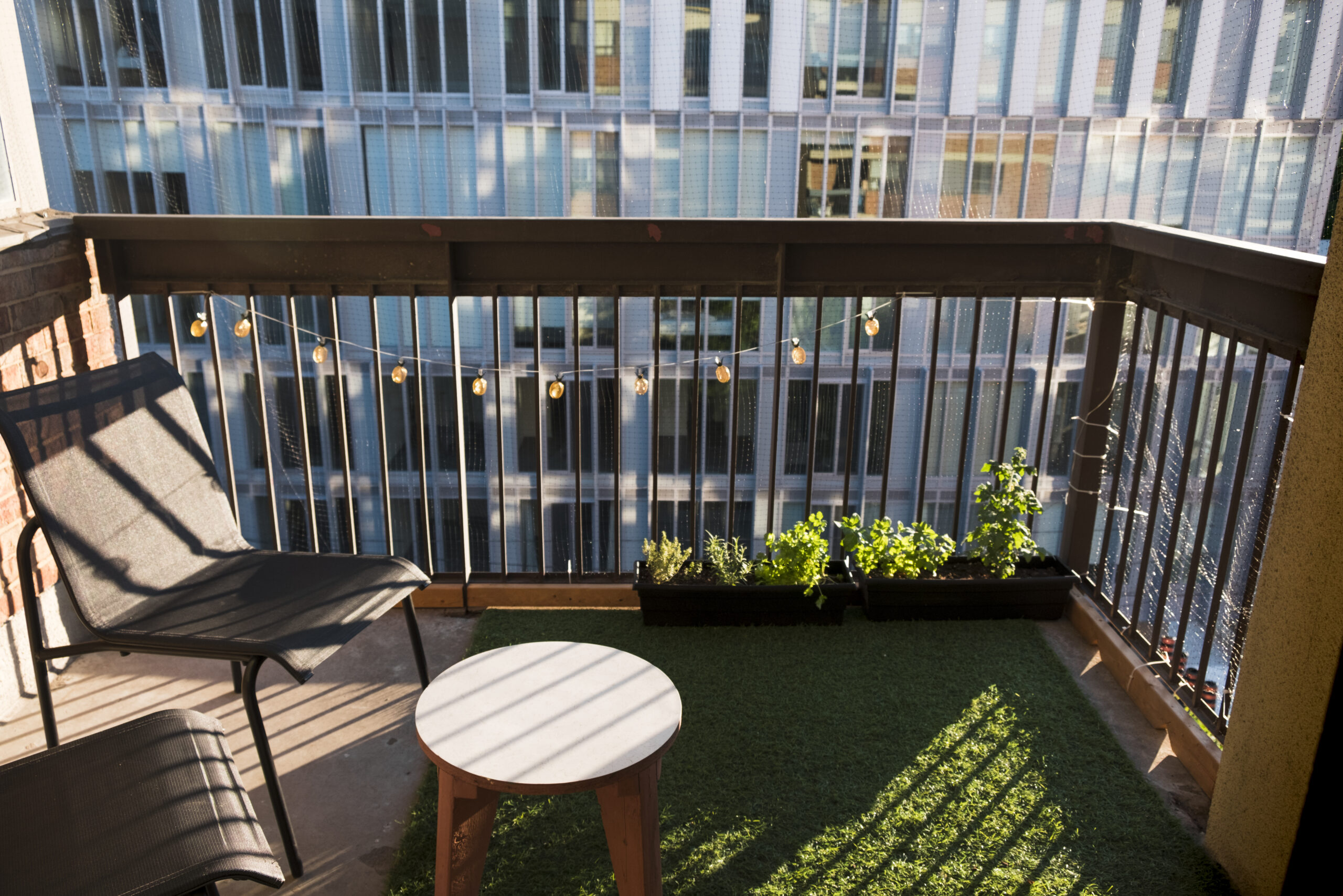 Apartment balcony in city with grass turf and potted plants. Evening light.